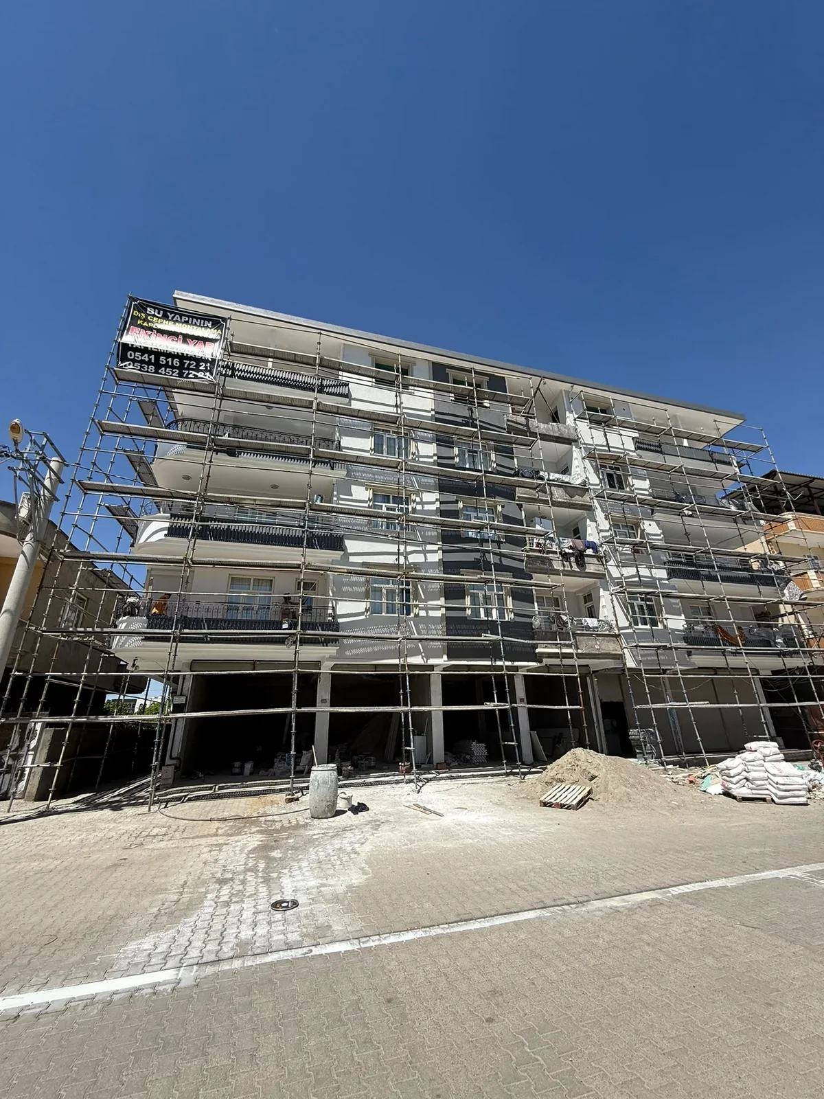 ASL YAPI — Cadde kenarındaki açık renkli balkonlu yapının cephesi boyunca uzanan iskele