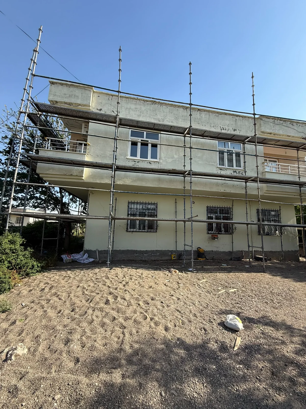 ASL YAPI — Pencere ve balkonları bulunan mevcut yapının yıpranmış sıvalı cephesi önündeki iskele